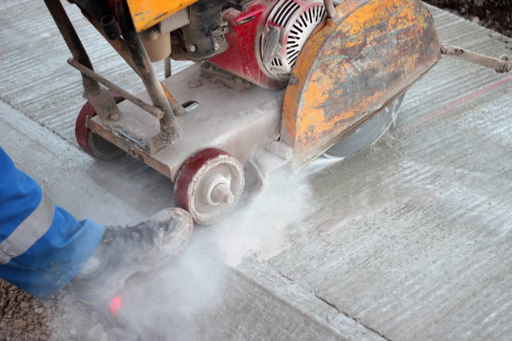 Worker using a diamond blade saw to cut expansion joints into asphalt pavement.