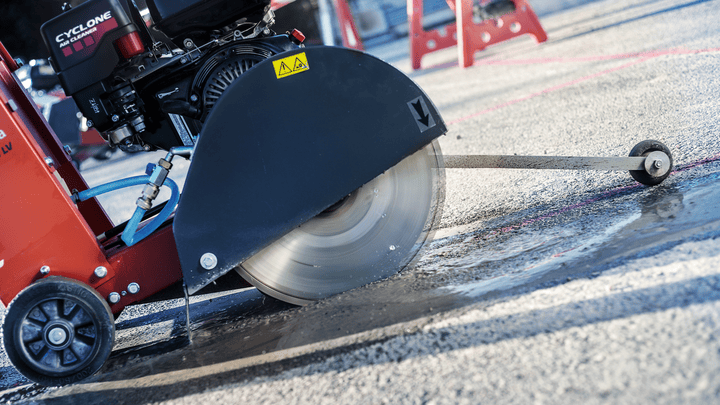 Worker using a diamond blade saw to cut expansion joints into asphalt pavement.