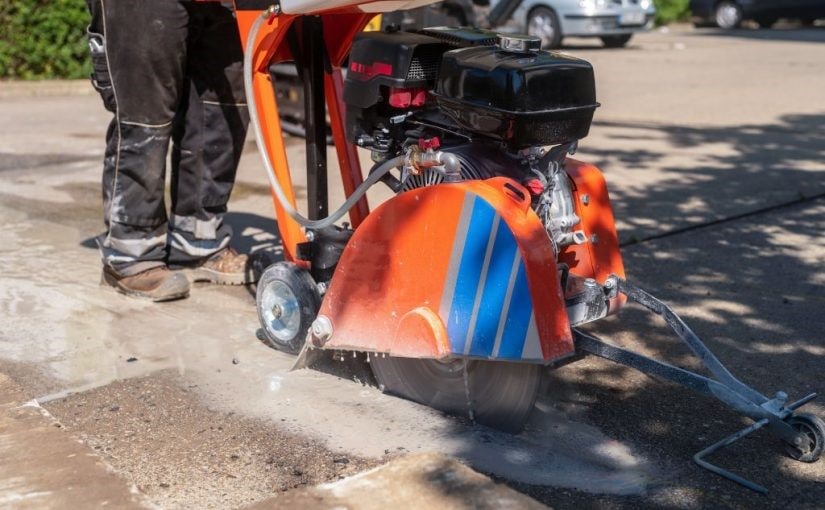 Worker using a diamond blade saw to cut expansion joints into asphalt pavement.