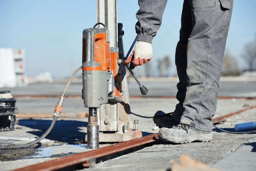 Close-up view of a heavy-duty concrete core drilling machine with a mounted diamond drill bit.